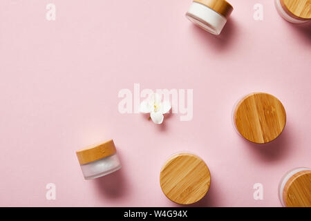 Blick von oben auf die verstreuten Gläser mit Creme- und Holz- kappen, und Jasmin Blume in der Mitte auf Rosa Stockfoto