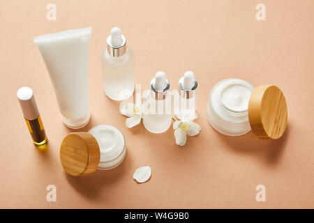 Mascara Flasche mit natürlichem Öl, Creme Tube, Kosmetik Glas Flaschen, Gläser mit Sahne und Jasminblüten auf beige Stockfoto