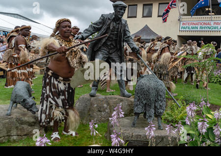 Zulu Krieger neben der Statue des Viehtreibers auf der Royal Welsh Showground in Llanelwedd. Besuch von König Goodwill der Zulu Nation auf der Royal Welsh Show (RWAS) in Builth Wells. Llanelwedd, Powys, Wales. Stockfoto