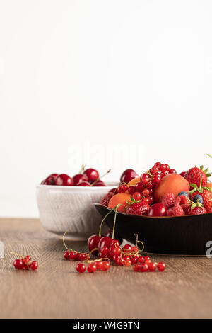 Selektiver Fokus der roten Kirschen in Weiß Schüssel und gemischte Beeren auf Platte auf Holztisch isoliert auf weißem Stockfoto