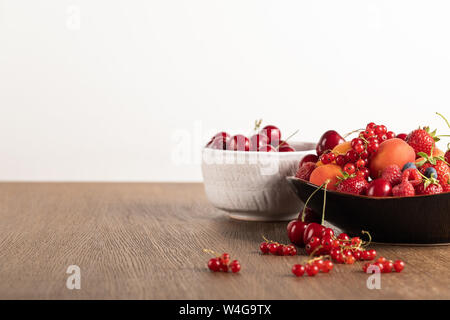 Selektiver Fokus von Kirschen in weiße Schüssel und gemischte Beeren auf Platte auf Holztisch isoliert auf weißem Stockfoto