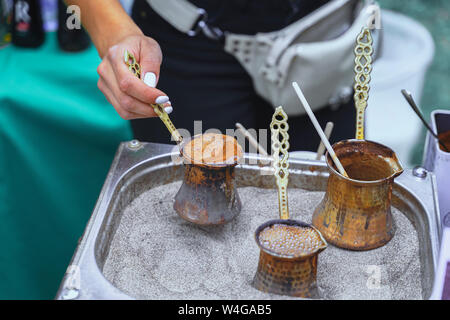 Hände von Mädchen kochen Kochen köstliche türkische aromatischen Kaffee mit Schaumstoff in Kupfer Türken an heißen Sand. Kaffee Vorbereitung Konzept Stockfoto