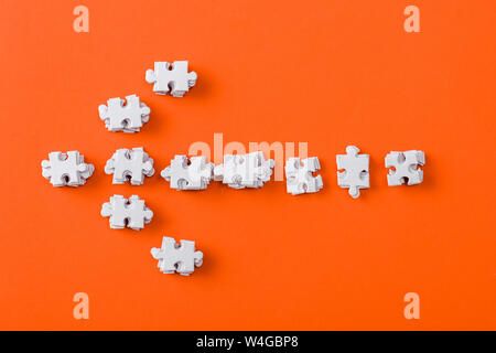 Blick von oben auf die weiße Richtung Pfeil mit Puzzle Stücke auf Orange Stockfoto