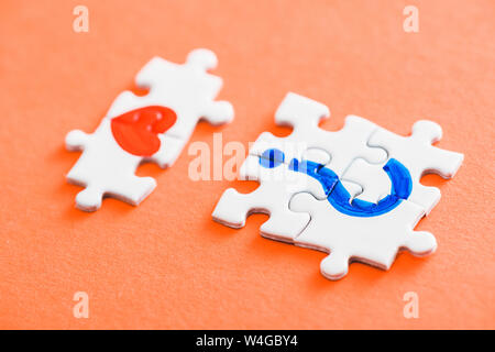 Selektiver Fokus der angeschlossenen Puzzleteile mit roten Herzen und blauen Fragezeichen auf Orange Stockfoto