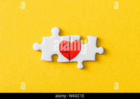 Blick von oben auf die angeschlossenen Puzzle Stücke mit roten Herzen isoliert auf Gelb Stockfoto