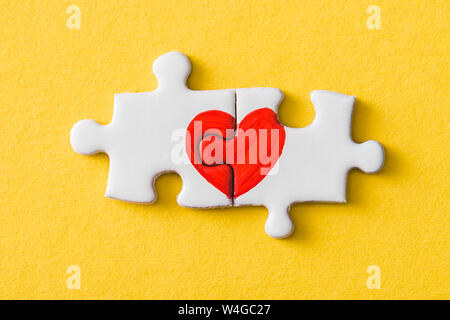 Blick von oben auf die angeschlossenen Puzzleteile mit roten Herzen isoliert auf Gelb Stockfoto