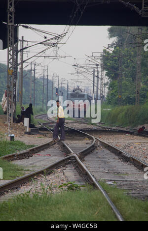 Man überqueren Bahngleise mit dem Zug im Hintergrund, Delhi, Indien Stockfoto