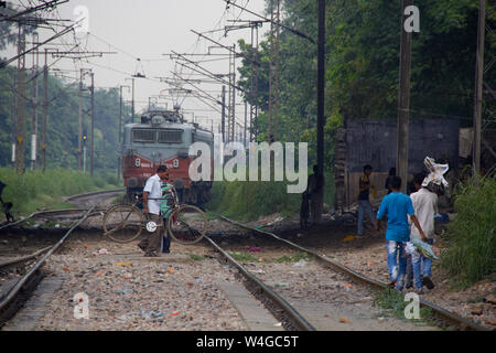 Gruppe von Menschen Kreuzung Eisenbahn tracks mit Zug im Hintergrund, Delhi, Indien Stockfoto