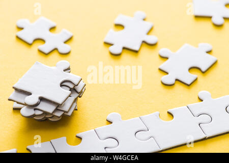 Selektiver Fokus der angeschlossenen Jigsaw in der Nähe von Stapel Puzzleteile auf Gelb Stockfoto