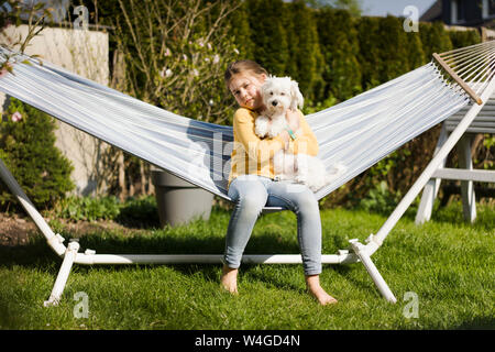 Portrait von Mädchen mit Hund in der Hängematte im Garten Stockfoto