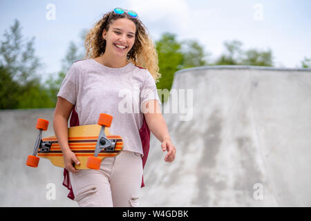 Lächelnde junge Frau mit einem Longboard in einem Skatepark Stockfoto