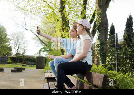 Zwei Mädchen sitzen auf einer Parkbank ein selfie Stockfoto