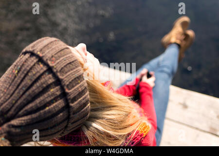 Junge blonde Frau mit Smartphone an einem See im Winter Stockfoto