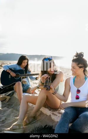 Junge Frau mit Freunden Gitarre spielen am Strand Stockfoto