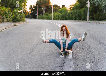 Junge Frau sitzt auf der Skateboard- und ihre Beine anheben Stockfoto
