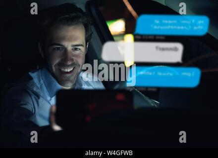 Lächelnd Geschäftsmann mit Mobiltelefon für Messaging ich im Auto in der Nacht Stockfoto