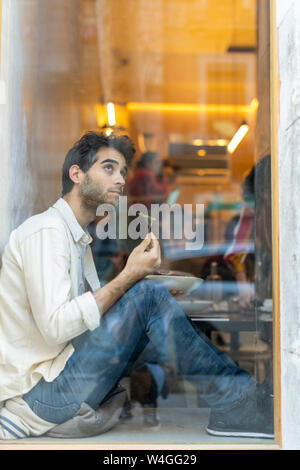 Mann essen einen Salat am Fenster sitzen in einem Restaurant mit Blick Stockfoto