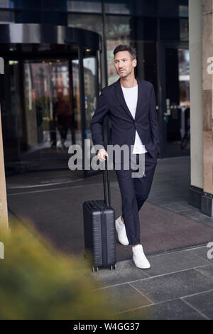 Reifer Mann mit Trolley vor einem Hotel Stockfoto