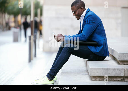 Junge Unternehmer trägt blaue Anzug Jacke, sitzen auf Schritt und Sie ihr Smartphone Stockfoto