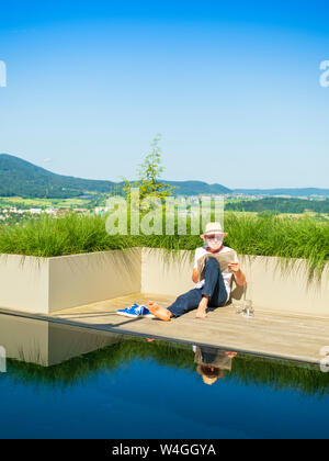 Senior Mann liest Zeitung am pool Stockfoto