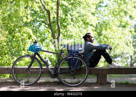 Junger Mann mit Fahrrad entspannend auf einer Bank Stockfoto