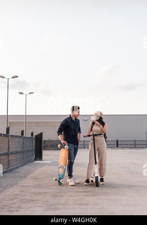 Junger Mann und Frau mit Longboard und Elektroroller mit Parkdeck Stockfoto