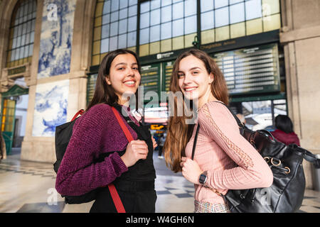 Portrait von zwei lächelnde junge Frauen mit Rucksäcken vor dem Bahnhof stehend, Porto, Portugal Stockfoto