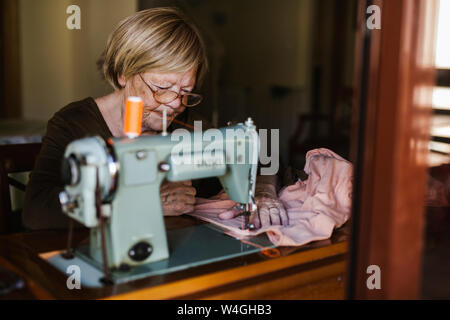 Ältere Frau mit einer Nähmaschine alte Maschine zu Hause Stockfoto