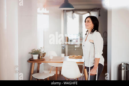 Reife Frau mit Krücken, allein zu Hause Stockfoto