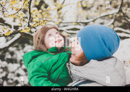 Porträt der kleine Junge seinen ersten Schnee auf den Armen seiner Mutter genießen. Stockfoto