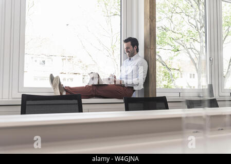 Junge Unternehmer sitzen auf Fensterbank, mit digitalen Tablet Stockfoto