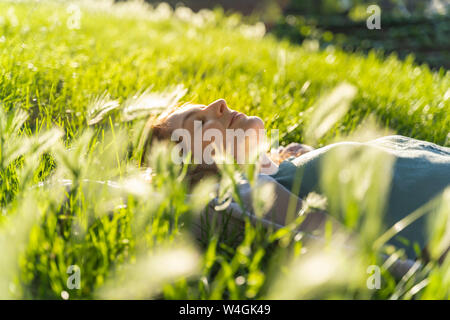 Junge rothaarige Frau liegend auf der Wiese im Park Stockfoto