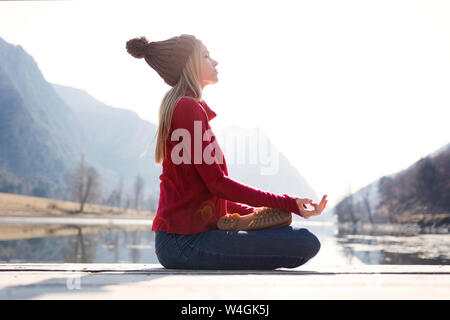 Blonde junge Frau sitzt auf der Jetty an einem See im Winter Stockfoto