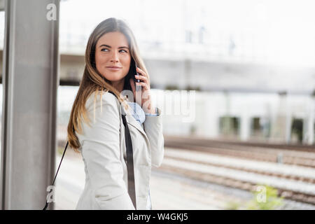 Junge Geschäftsfrau mit Smartphone, stehend auf Station Stockfoto