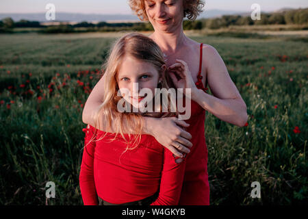 Die Mutter streichelte daughte Haar, stehend in einem Mohnfeld Stockfoto