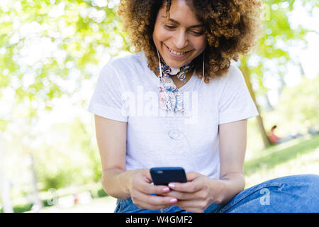 Lächelnde Frau mit Handy- und Ohrhörer in Park Stockfoto