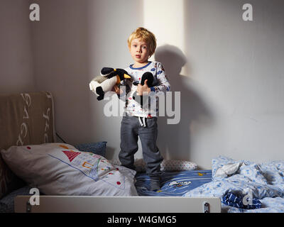 Porträt der kleine Junge stehend auf Bett mit seiner weichen Spielzeug Stockfoto