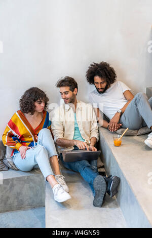 Drei Freunde sitzen auf Treppen mit Laptop und Trinken Stockfoto