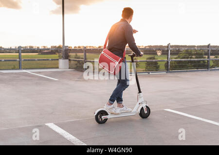 Junger Mann mit Handy und Elektroroller auf Parkdeck bei Sonnenuntergang Stockfoto