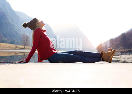 Blonde junge Frau sitzt auf der Jetty an einem See im Winter Stockfoto