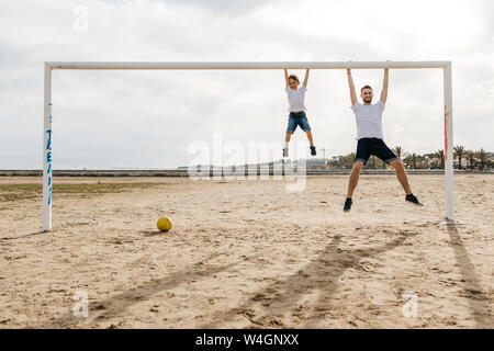 Mann und der Junge hängt von dem Ziel, beim Fußballspielen am Strand