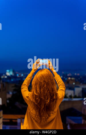 Junge Frau mit Smartphone auf einem Aussichtspunkt an der blauen Stunde, Barcelona, Spanien Stockfoto