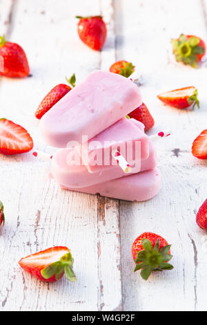 Gestapelte hausgemachtes Erdbeer Joghurt Eis am Stiel mit frischen Erdbeeren auf weißem Holz Stockfoto