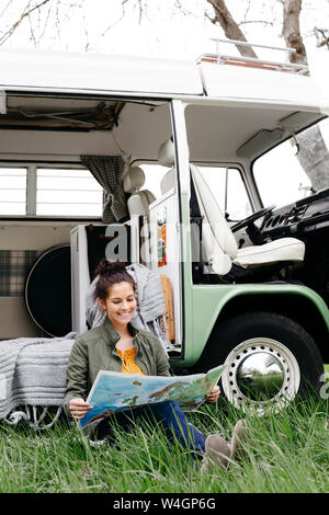 Junge Frau Studium Karte, im Gras sitzen, vor ihr Wohnmobil Stockfoto