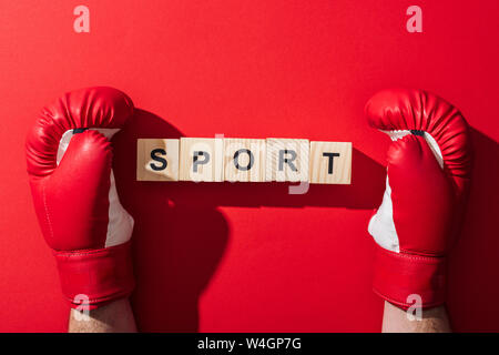 7/8-Ansicht des Menschen in Boxhandschuhe in der Nähe von Holzwürfel mit Sport Schrift auf Rot Stockfoto