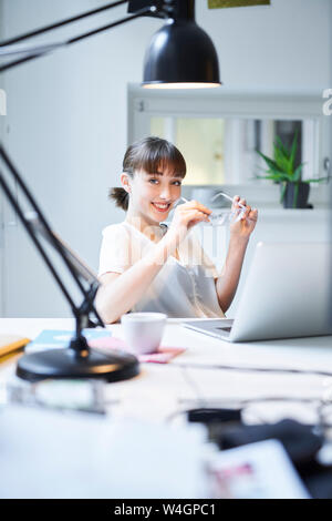 Portrait von lächelnden Jungen geschäftsfrau am Schreibtisch sitzen in einem Büro Stockfoto