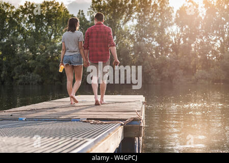 Junges Paar Hand in Hand auf Steg an einem entfernten See Stockfoto
