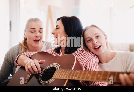 Reife Frau mit zwei Töchtern singen und Gitarre spielen zu Hause Stockfoto