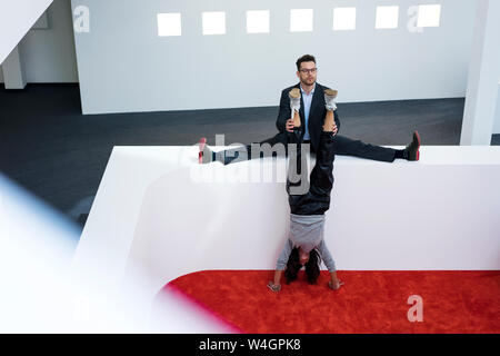 Unternehmer im Amt, die Beine der Frau macht einen Handstand Stockfoto