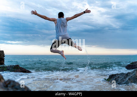 Rückansicht des jungen Mannes in der Luft am Meer springen Stockfoto